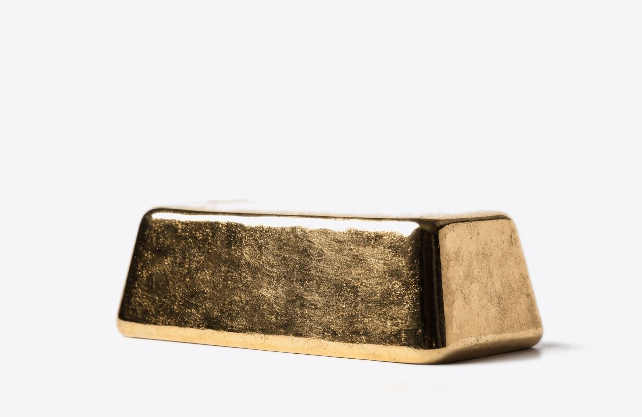 A single cast gold bar resting on a pale surface.